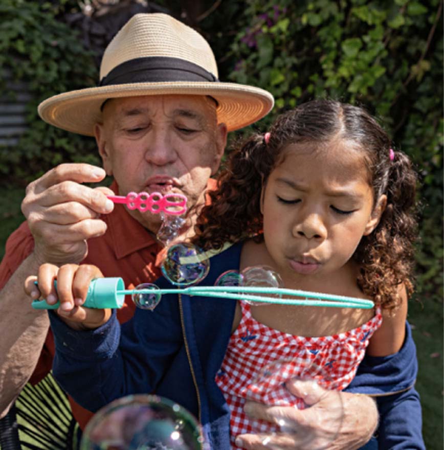 Grandfather and granddaughter blowing bubbles outdoors